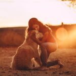 young-woman-hugging-golden-retriever-dog-in-countryside-at-sundown