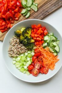 vegetable salad in a bowl beside a chopping board with tomatoes and cucumber