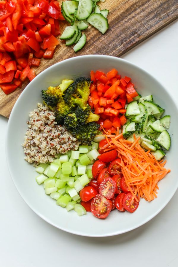 vegetable salad in a bowl beside a chopping board with tomatoes and cucumber